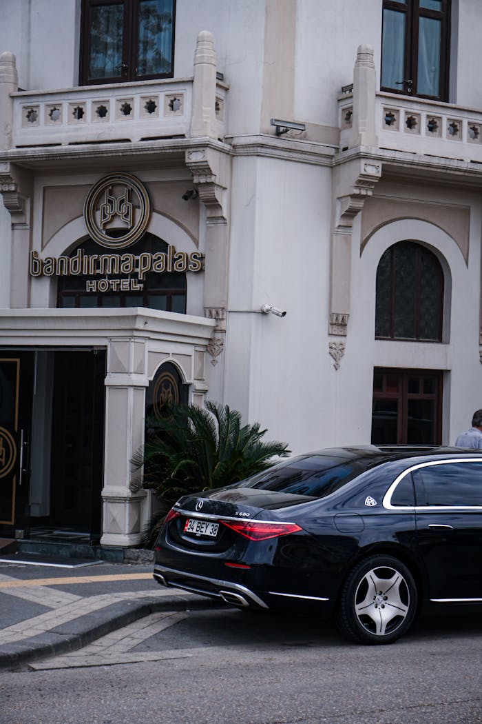 A luxury car parked in front of the historic Bandırma Palas Hotel, Turkey, showcasing urban architecture.
